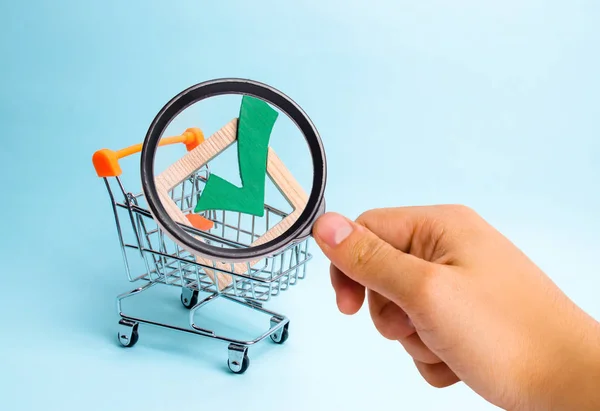 Magnifying glass is looking at the wooden checkmark for voting on elections in a supermarket trolley. Lobbying interests, election corruption voter bribery, and rigging election results.