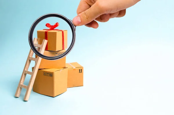 Magnifying glass is looking at the gift box on a pile of boxes. The concept of finding the perfect gift. Limited offer Buy a gift on time. Sale, big discounts and excitement before the holidays.