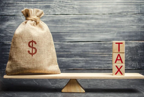 Money bag and wooden blocks with the word Tax on the scales. The concept of paying taxes and debt repayment. Register of taxpayers for property. Property taxes and mortgages.