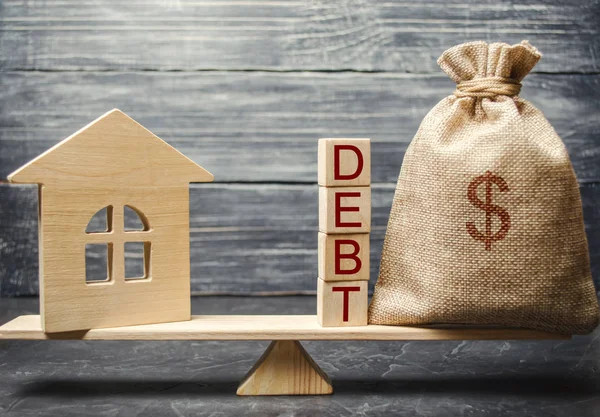 Money bag and wooden blocks with the word Debt and a miniature house on the scales. Payment of debt for real estate. Pay off the mortgage loan. Risks of buying a house. Buying an apartment on credit.