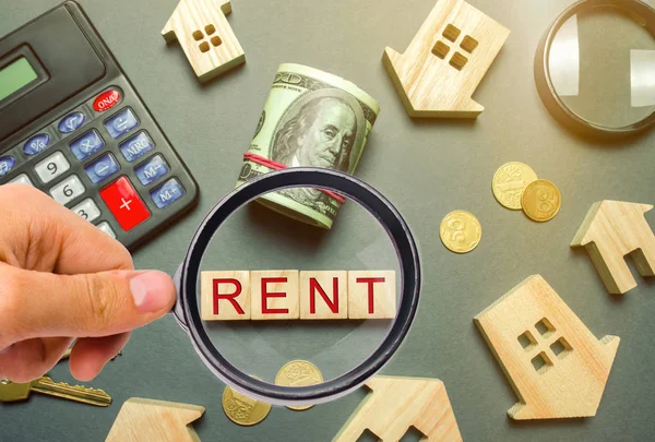 Table with wooden houses, calculator, coins, magnifying glass with the word Rent. The concept of rental housing. Rent an apartment or house. Payment for rent. Real Estate Agent Services. Realtor