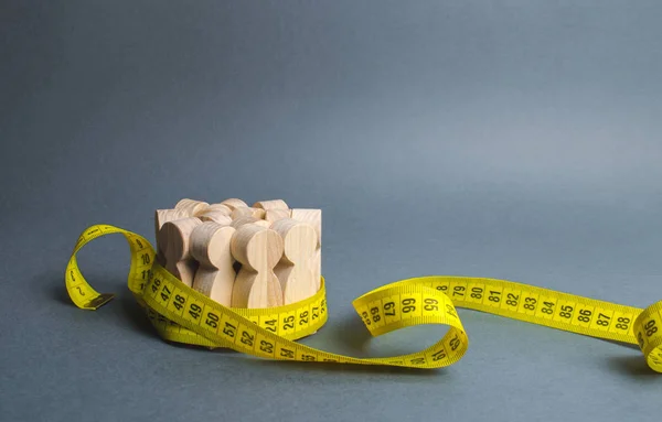 A crowd of wooden figures Gripped by measuring tape. Information statistics, measurement of the number, trends of population growth. Social Sciences. Promotion of ideas for weight loss, lifestyle