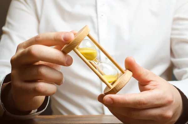 Hourglass in the hands of a businessman in a white shirt. Planning time and reducing business costs. Catch all and do all planned things. Time saving. Businessman in thought. The minimum wage per hour