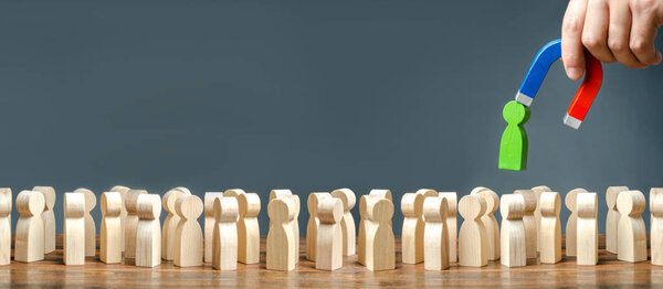 Рука с магнитом вытаскивает зеленую человеческую фигуру из большой толпы людей. Привлечение новых работников, кадровиков. Поиск талантливых работников с большим карьерным потенциалом. Отбор. пространство для копирования баннера
