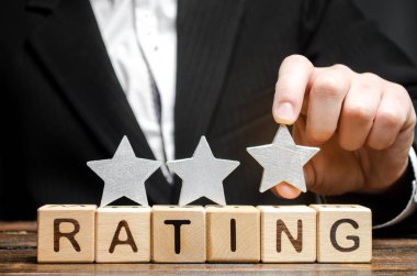 İşadamı, üçüncü yıldızı tahta bloklarda sınıflandırma kelimesinin üstüne koyuyor. Hizmet kalitesi kavramı. Otel ya da restoran derecesi. Eleştirmenlerin ve ziyaretçilerin değerlendirilmesi. İyi kalite. Geri bildirim. Üç.