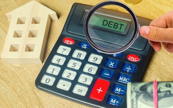 Money and houses on the table and a calculator with the word Debt. The concept of buying property in debt. Analysis of costs and revenues. Apartment purchase. Selling a house. Credit and mortgage.