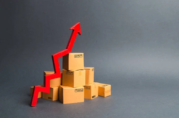 段ボール箱の山と赤い上矢印。財・製品の生産の伸び率は、経済指標の増加である。消費者需要の増加、輸出の増加、輸入。売上高の増加 — ストック写真