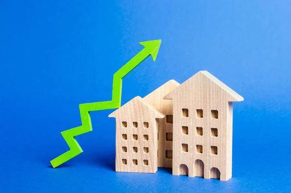 Figuren van residentiële gebouwen en groene pijl omhoog. Stijgende waarde en prijs. Appartementen te koop. Groei van de vraag en liquiditeit voor onroerend goed, stijging van de tarieven voor het onderhoud van gebouwen. — Stockfoto