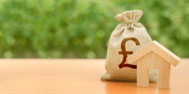 Ahşap ev heykelcik ve doğanın arka planda pound sterlin para çantası. Bütçe, sübvansiyonlu fonlar. Konut satın almak için mortgage kredisi, inşaat veya modernizasyon. Vergi, bina bakımı.