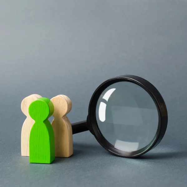 Three wooden human figure stands near a magnifying glass on a gray background. The concept of the search for people and workers. Search for vacancies and work. Human resources, management.
