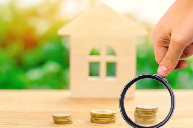 A magnifying glass explores a stack of coins and a wooden house. Real estate concept. deposit interest rates, mortgage interest. Affordable housing. Rent and monthly payment. Selective focus clipart