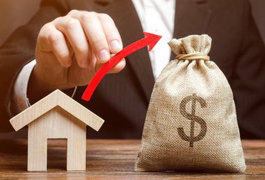 Bir para çantası ve evin yanında bir adamın elinde kırmızı bir ok. Gayrimenkul piyasasıbüyüme kavramı. Fiyat artışı. Bir ev veya daire satın almak için artan talep. Mortgage oranları artış