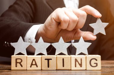İşadamı ahşap bloklar üzerinde kelime Rating üzerinde beşinci yıldız koyar. Otel ve restoranların yüksek derecelendirme kavramı. Eleştirmenlerin ve ziyaretçilerin değerlendirilmesi. Kalite seviyesi, iyi hizmet