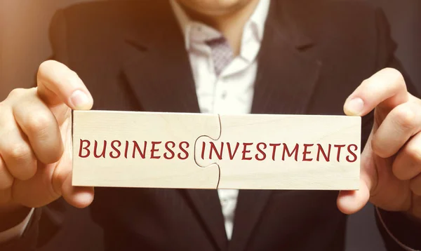 Businessman collects wooden puzzles with the words business investments. Increase capital. Investing your assets in your own or someone else's business. Profit in the short or long term. Investor