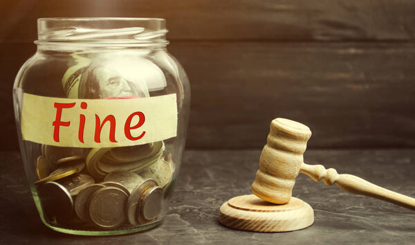 Glass jar with the word Fine and the judge's hammer. Penalty as a punishment for a crime and offense. Financial punishment. Violations of traffic laws. Fraud. Fines can also be used as a form of tax