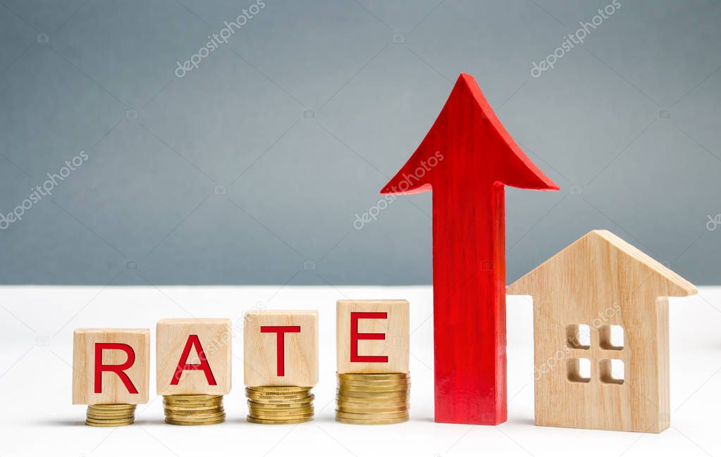 Wooden blocks with the word Rate, up arrow and wooden house. The concept of raising interest rates on mortgages. Growing interest on the loan. Rates are a type of property tax system