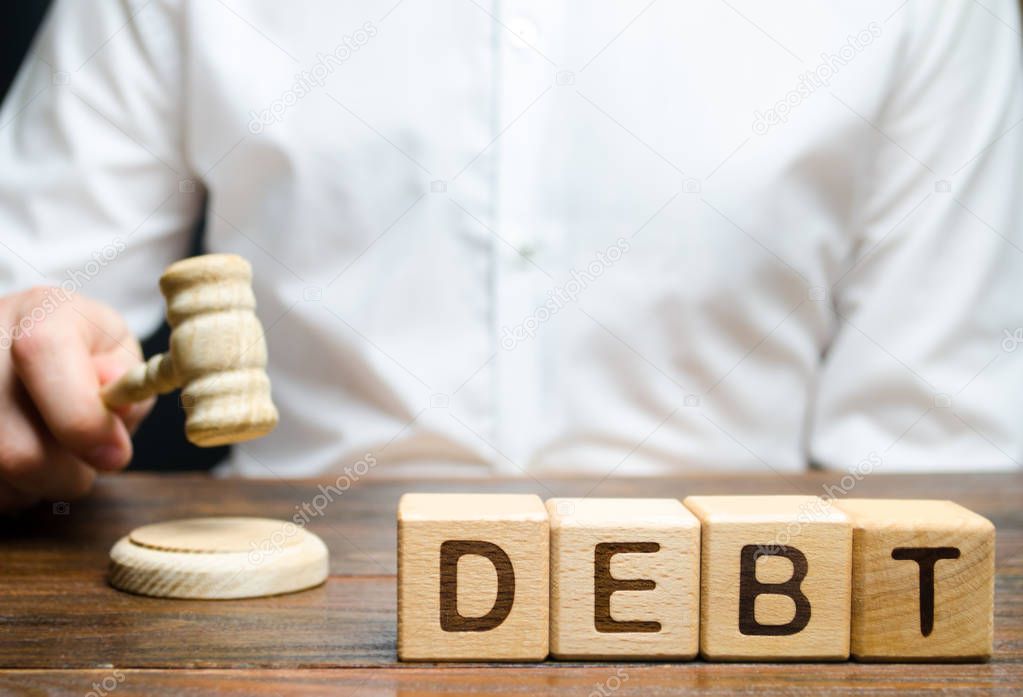 Wooden blocks with the word Debt and judge with a gavel. The concept of judicial punishment for non-payment of debt. Property debts. Tax evasion / avoidance. Bankruptcy and financial crisis