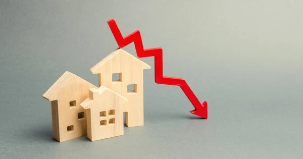 Casas de madera miniatura y una flecha roja hacia abajo. El concepto de bienes raíces de bajo costo. Tasas de interés hipotecarias más bajas. La caída de los precios de alquiler de viviendas y apartamentos. Reducción de la demanda de compra de vivienda — Foto de Stock