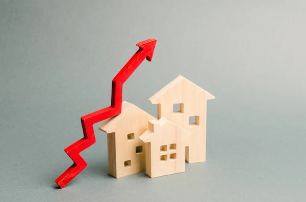 Casas de madera en miniatura y flecha roja arriba. El concepto de aumentar el costo de la vivienda. Gran demanda de bienes raíces. El crecimiento de la renta y las tasas hipotecarias. Venta de apartamentos. La población crece — Foto de Stock