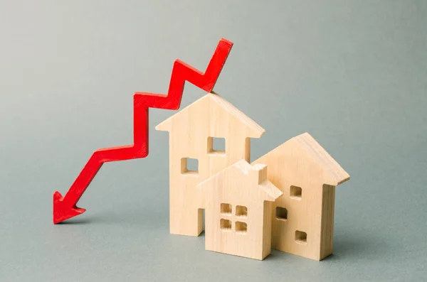 Casas de madera miniatura y una flecha roja hacia abajo. El concepto de bienes raíces de bajo costo. Tasas de interés hipotecarias más bajas. La caída de los precios de alquiler de viviendas y apartamentos. Reducción de la demanda de compra de vivienda —  Fotos de Stock