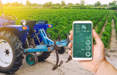 A hand is holding a smartphone with infographics on background of tractor and Bulgarian pepper plantation. Farming and agriculture. Agricultural machinery, data analyzing on plants status. harvesting clipart