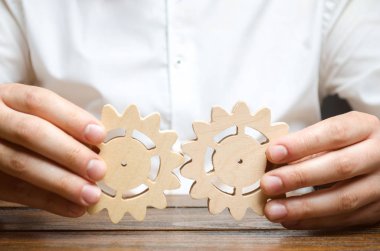 Businessman in white shirt connects two wooden gears. Symbolism of establishing business processes and communication. Improving work efficiency, establishing new connections and suppliers. clipart