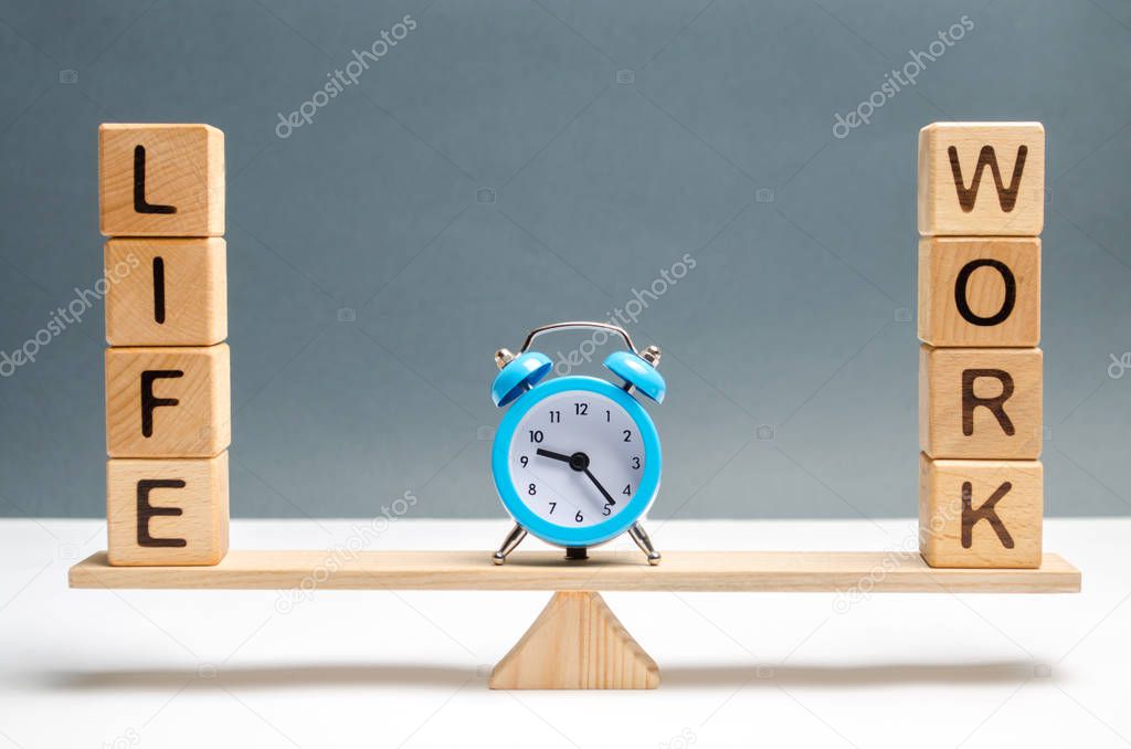 Blue clock between the words life and work on the scales. choice between life and work. The concept of paying attention to the life values, promotion at work, overtime and exhausting work.