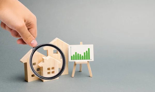 Loupe de verre regarde les maisons en bois avec un stand de graphiques et d'informations. Demande croissante de logements. croissance de la ville et de sa population. Investissements. hausse des prix. Concentration sélective — Photo