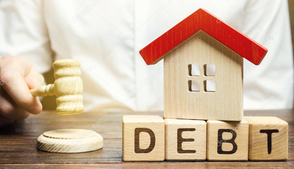 Wooden blocks with the word Debt and a miniature house with a judge's hammer. Confiscation of property for failure to pay the debt. The withdrawal of housing. Moratorium. Criminal penalty