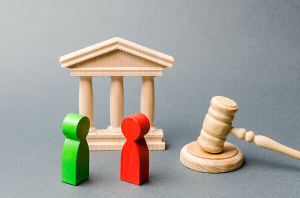 Wooden figures of people standing near the judge's gavel. Litigation. Business rivals. Conflict of interest. Law and justice. The layer's services. Two opponents. Judgment. Gavel. Red and green