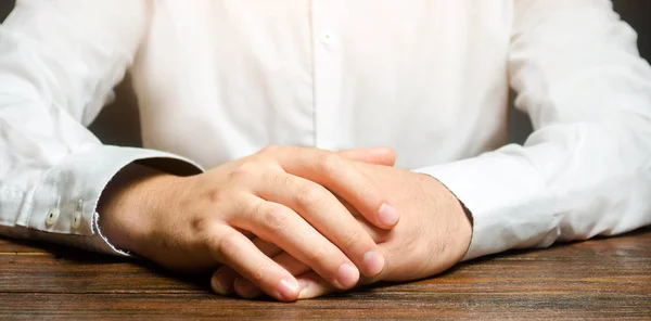 Un hombre se sienta a la mesa con los brazos cruzados. Listo para escuchar noticias y críticas. Hablar en serio. Calmadamente. Comunicación y expresiones corporales. entrevista de trabajo —  Fotos de Stock