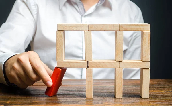 The man removes the red structural element, which will collapse. Destruction of a complex structure by negligence. Incompetent businessman. Loss of key elements and employees. Damage to the opponent. — Stock Photo, Image