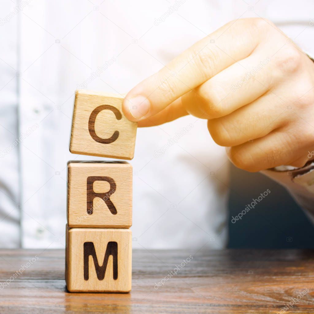 Wooden blocks with the word CRM (Customer Relationship Management) and businessman. Automation strategies for interacting with clients. Increase sales, optimize marketing and improve customer service