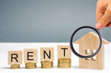 Büyüteç, Rent kelimesi ile ahşap bloklar, sikkeler ve minyatür bir ev. Konut ve gayrimenkul kiralama kavramı. Kiralık bir ev veya daire maliyeti. Para biriktirip. Kiralama.