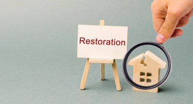 Restorasyon yazıtlı bir poster ve kırık ahşap bir ev. İkincil konutları onarın. İyileştirme süreci, evin yeniden inşası. Yangın veya doğal afet sonrası iyileşme