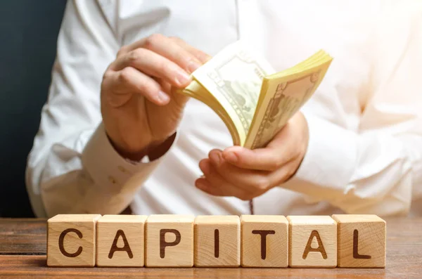 Businessman counts money on the background of the caption Capital. Capitalism, capital increase and influence. Financial liberalization of developing countries, unprincipled withdrawal of capital.