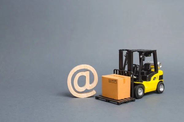 Yellow Forklift truck carries a cardboard box near a email symbol commercial AT. development of Internet network trade. E-commerce. sales of goods through online trading platforms. shopping online.