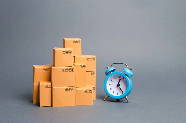 Lots of cardboard boxes and a blue alarm clock. Express delivery concept. Temporary storage, limited offer and discount. Optimization of logistics and delivery, improving transportation efficiency