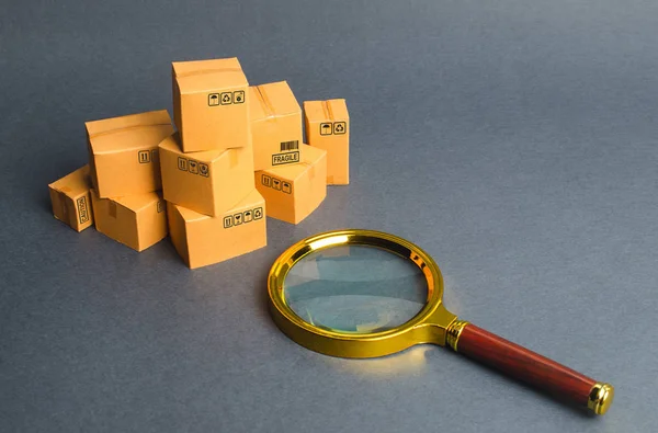 A pile of boxes and a magnifying glass. Concept search for goods and services. Tracking parcels via the Internet. Quality control. Searching for customers, sales and retail. Register of tenders