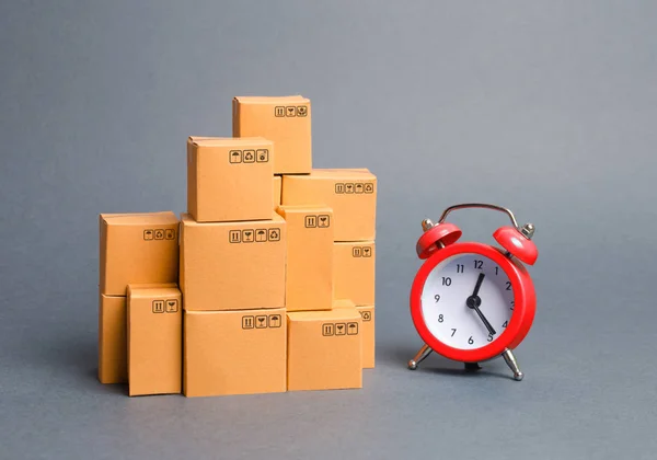 Lots of cardboard boxes and a red alarm clock. Express delivery concept. Optimization of logistics and delivery, improving transportation efficiency. Temporary storage, limited offer and discount. — Stock Photo, Image
