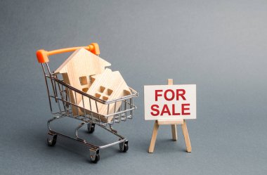 Bir ticaret sepeti ahşap evler ve Satılık yazıt lı bir stand. Ev ve emlak satışı. Büyük indirimler ve cazip terimler. yükselen fiyatlar veya kiralama. emlak piyasasında patlama