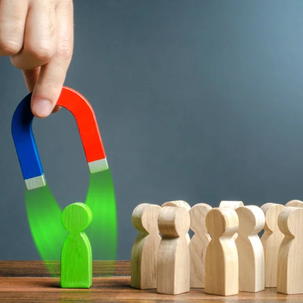 Una mano con un magnete sta cercando di tirare una figura verde vicino alla folla di persone. Reclutamento di nuovi lavoratori. Formazione di un nuovo team aziendale. Ricerca di lavoratori di talento con grandi potenzialità di carriera . — Foto Stock