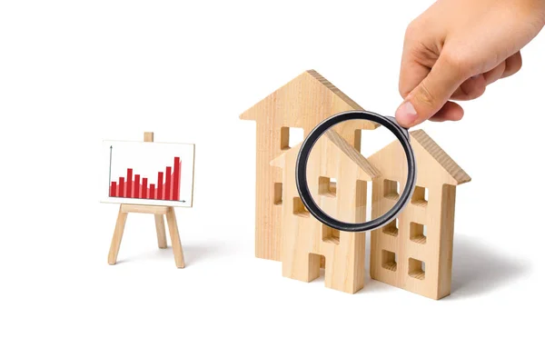 Vergrootglas is kijken naar de houten huizen met een standaard van graphics en informatie. Groeiende vraag naar woningen en vastgoed. Statistieken over de marktsituatie. Investeringen. — Stockfoto