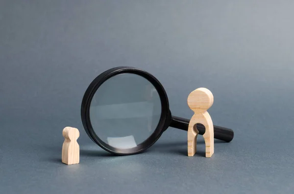 A wooden figure of a woman with emptiness and a child stands near the magnifying glass. The concept of finding a child, the adoption of children. Mother lost her baby and is now looking for him.