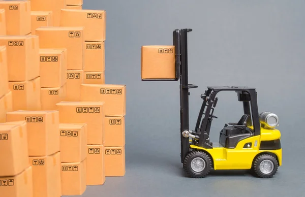 Sárga targonca csákány egy doboz egy halom dobozok. Áruk raktároztatása raktárból, szállításból és szállításból. Teherszállítás, szállítás. Import és export, árucsere — Stock Fotó