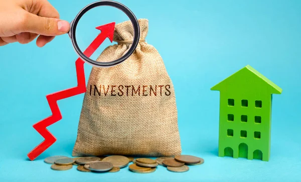 Sac d'argent avec le mot Investissements, flèche vers le haut et maison en bois. Le concept d'investissement dans la construction immobilière. Investissement efficace. Acheter des appartements. Entreprises et finances — Photo