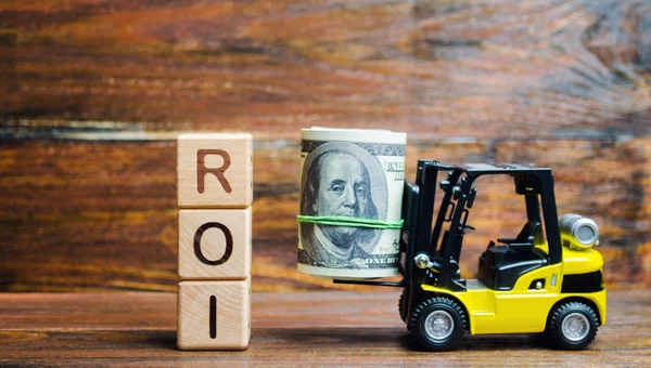 Wooden blocks with the word ROI and money with forklift. Ratio between the net profit and cost of investment resulting from an investment of resources. High level of business profitability.