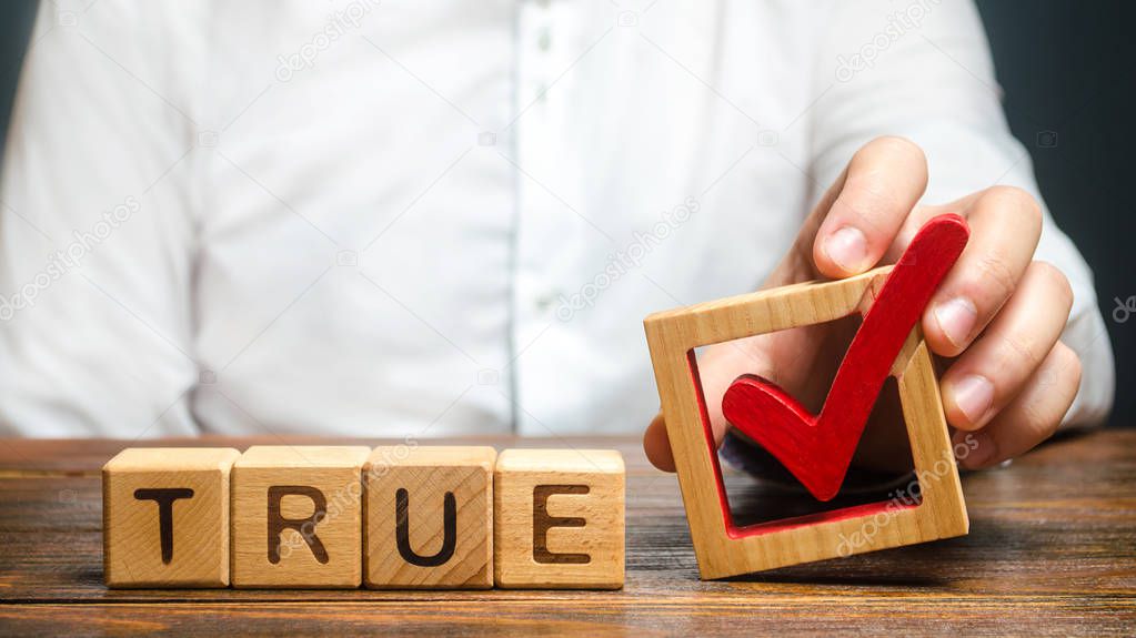 A man holds a red check mark over word True. Confirm the veracity and truth. Fight against fake news hostile propaganda. Confirmation facts, refutation of rumors. Debunking Myths and Misconceptions