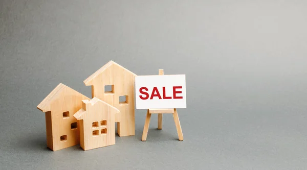 Three wooden houses and a stand with the inscription SALE. selling a home. Announcement of the sale and attracting potential buyers. Advertising campaign. purchase of real estate. — Stock Photo, Image