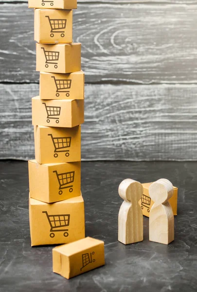 Two wooden people stand near a tower of boxes. buyer and seller, manufacturer and retailer. Discussion of the terms of the trading deal, the purchase of goods and services. Business and commerce. — Stock Photo, Image